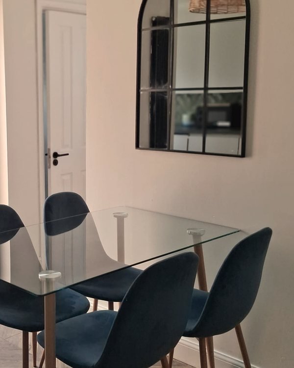 The dining area at Oasis House: a glass table and four soft blue chairs below an arched window-style mirror.