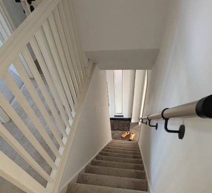 The staircase at Oasis House: a white spindle balustrade, soft carpet, and a pair of shoes left at the foot of the stairs.
