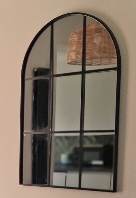 An arched mirror on the dining-area wall, reflecting the kitchen worktop and one of the rattan pendant shades.