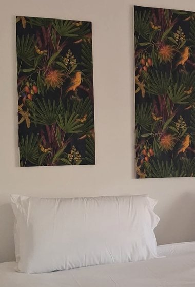 A bedroom corner: two dark botanical wall panels above white bedding and a single pillow.