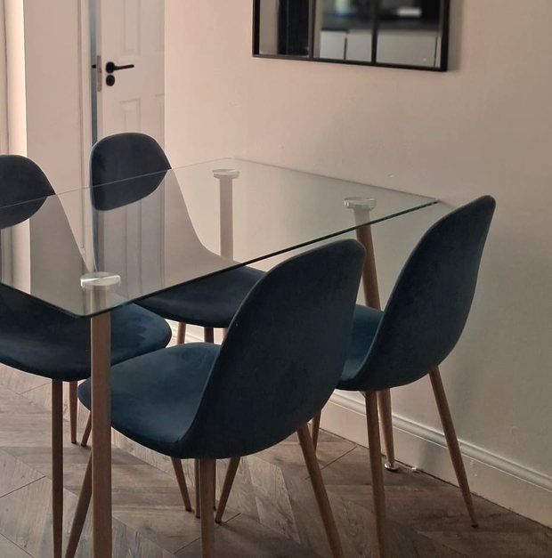 The dining area: a glass table with four blue velvet chairs on a herringbone floor.