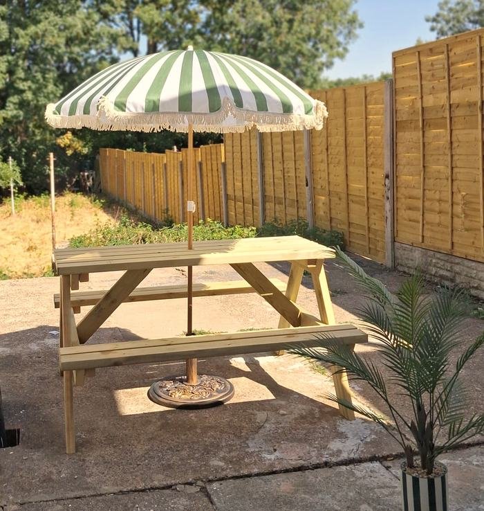 A wooden picnic bench under a green and white striped parasol on the paved area of the enclosed rear garden.