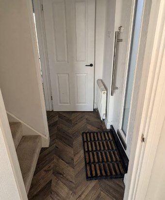 The downstairs hallway with a striped doormat, herringbone floor, radiator and a closed internal door.