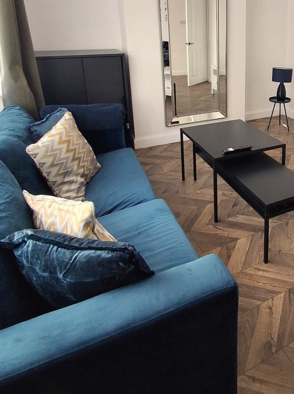 The sitting room at Oasis House: a blue sofa with patterned cushions, a tall mirror, two low tables and a herringbone wooden floor.