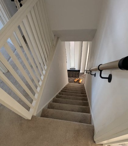 The carpeted staircase and white banister, looking down towards a pair of small yellow shoes by the front door.